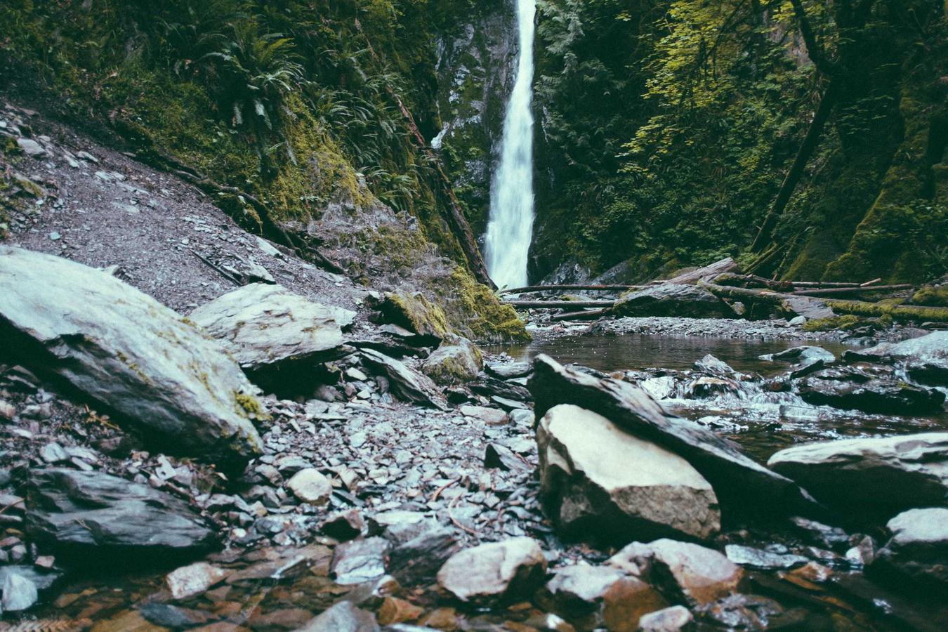 Cascada estrecha cayendo entre rocas grises y vegetación