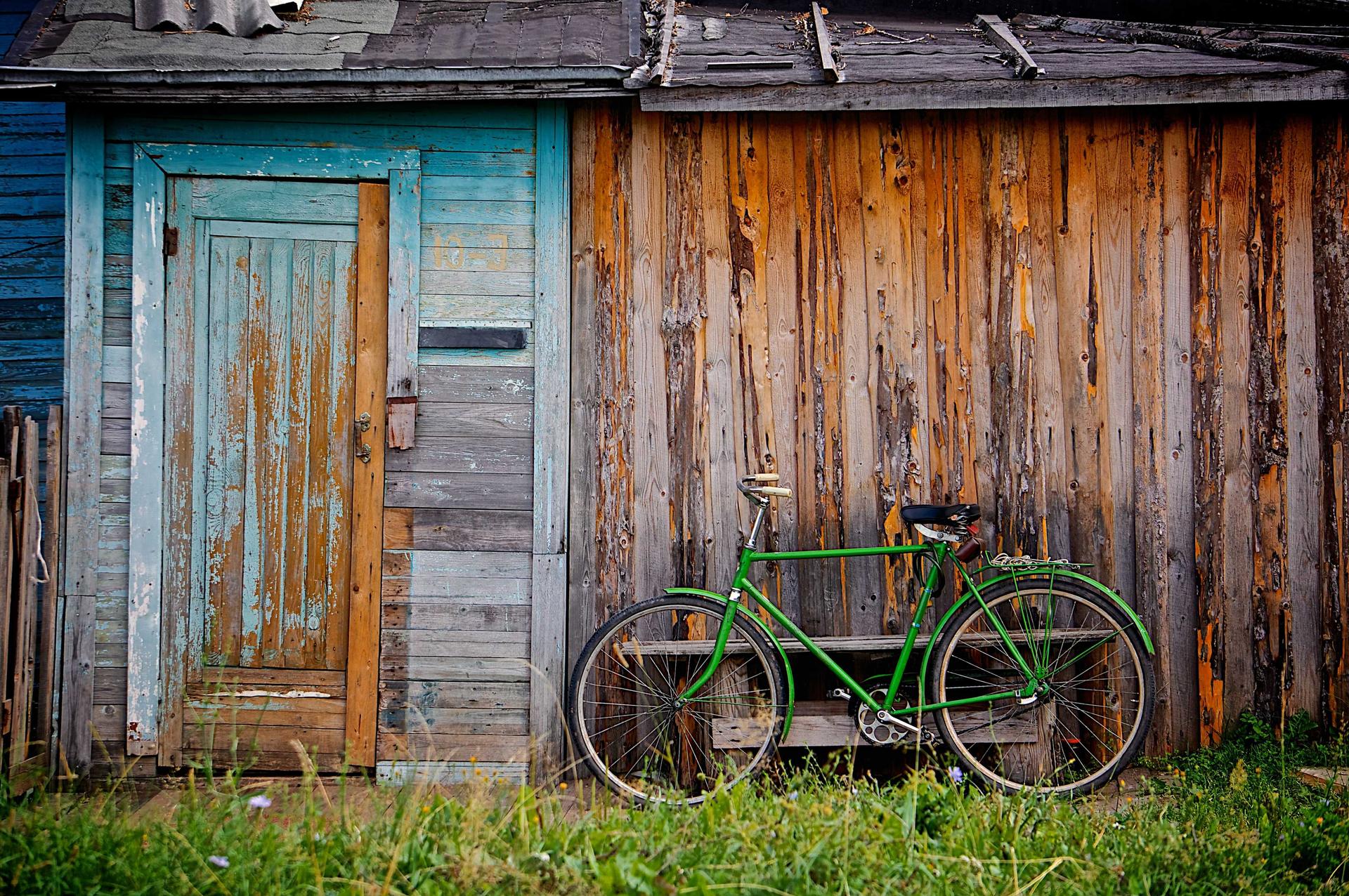 Bicicleta verde apoyada en la pared de madera de una cabaña